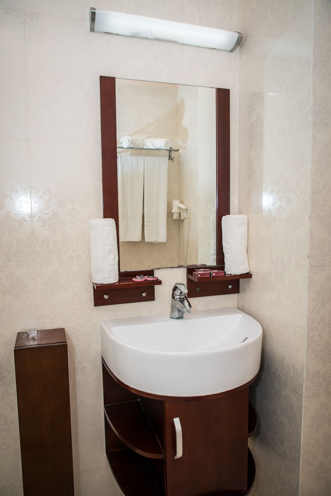 A bathroom with a white sink, a mirror with a wooden frame, and two towel racks with white towels.