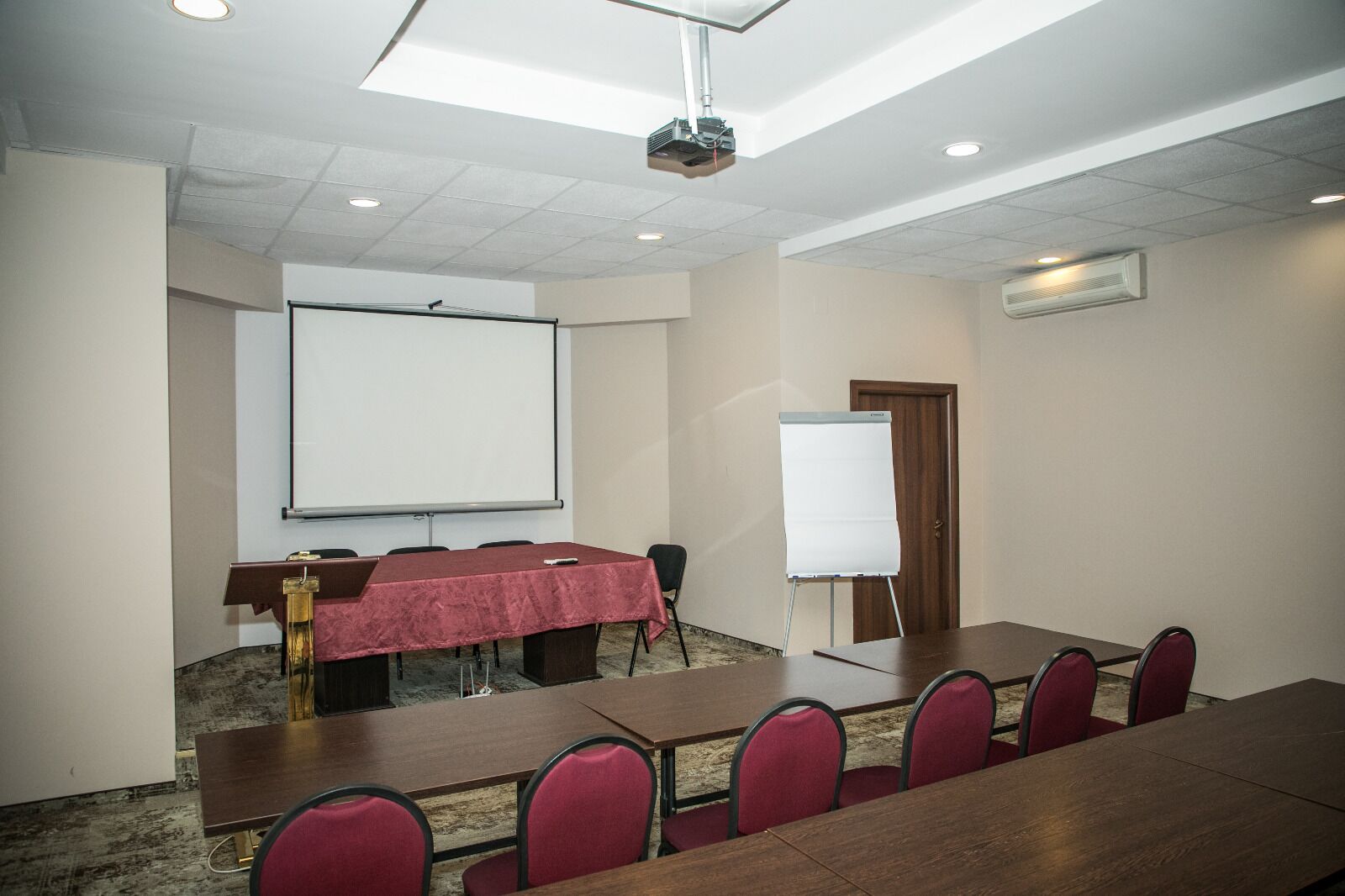 A conference room with a long table, red chairs, a whiteboard, and a projector.