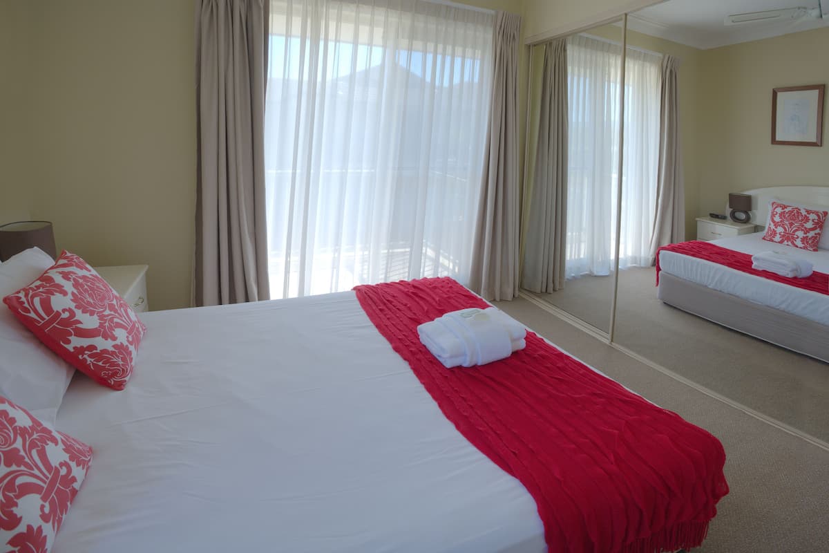 Una habitación de hotel con una cama grande, una mesita de noche, una lámpara y un espejo.