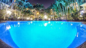 Una vista notturna di una piscina circondata da palme e edifici di un hotel.