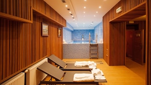 Un cuarto de spa con paneles de madera, pared de azulejos azules, una pequeña piscina y dos sillas reclinables con toallas.