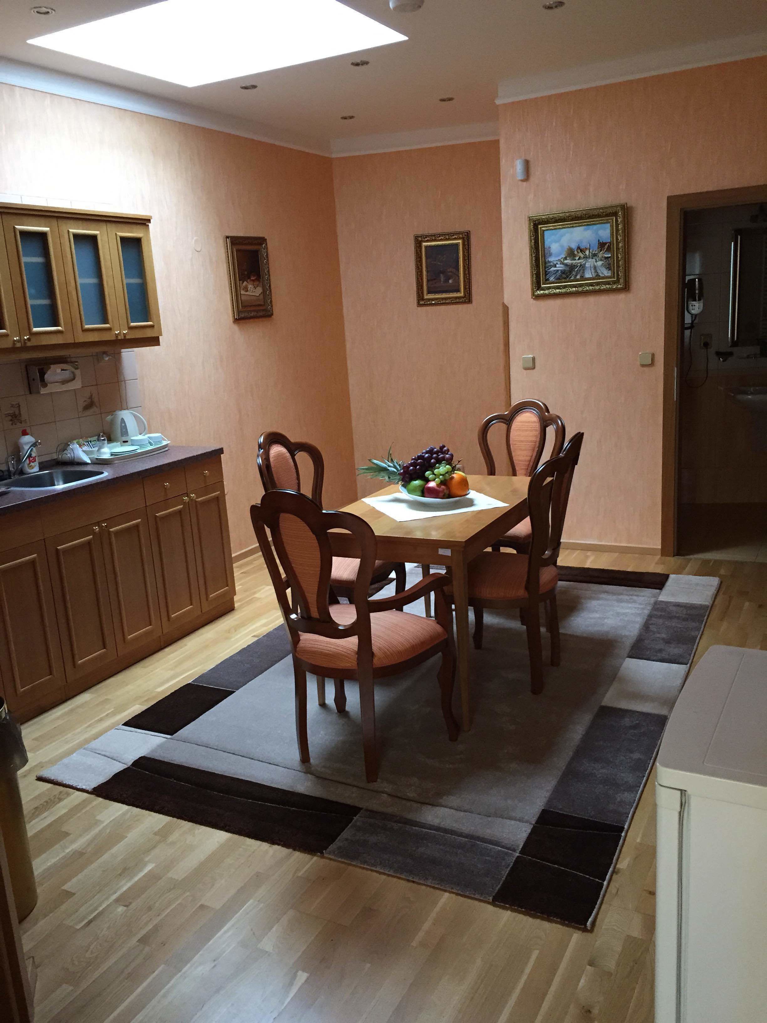 Un comedor con una mesa y sillas de madera, un frutero y una cocina con armarios de madera y una encimera.