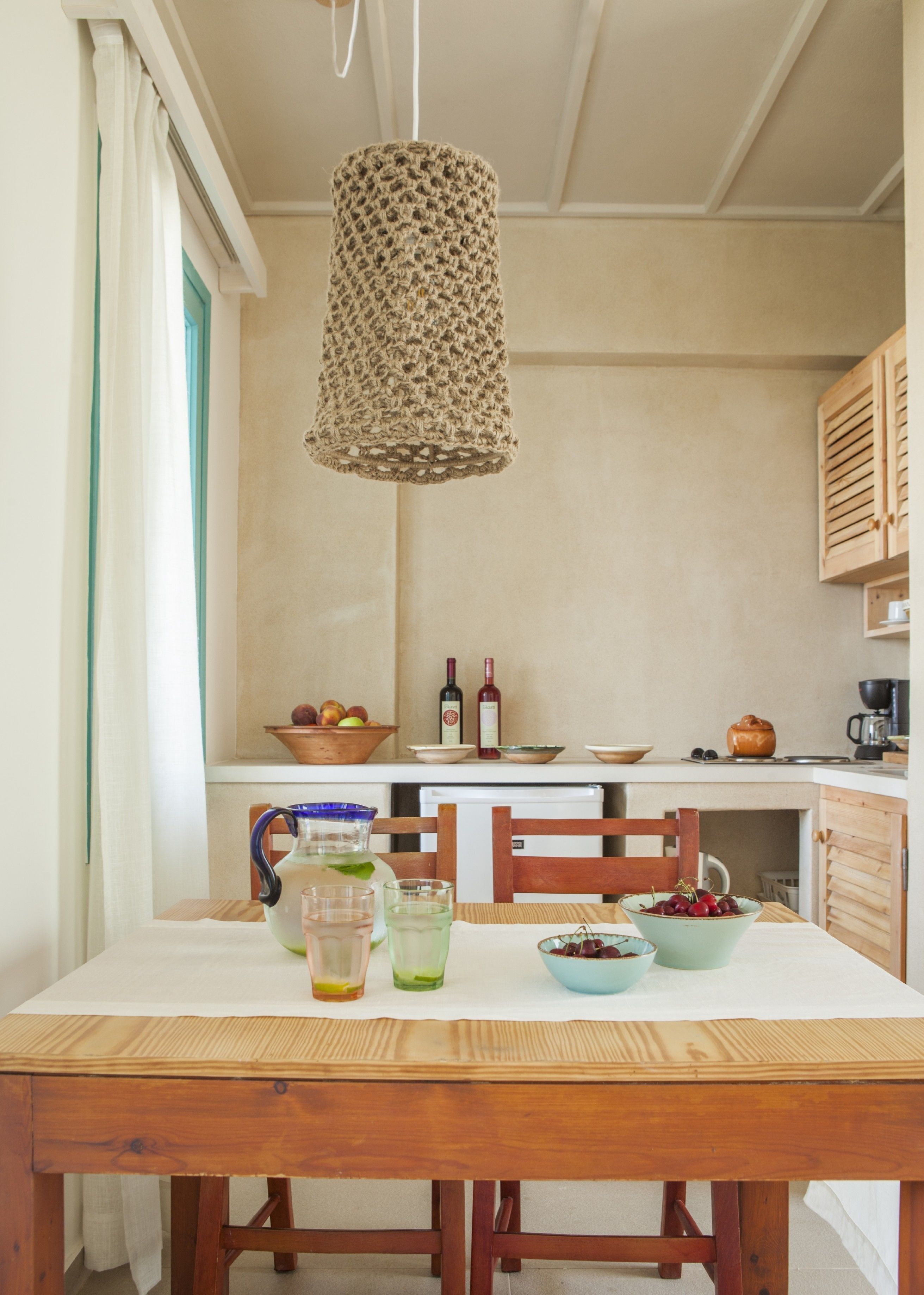 A kitchen with a wooden table, chairs, a hanging light fixture, and various kitchen items.