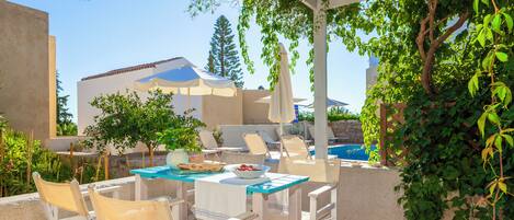 An outdoor patio with white furniture, a pool, and a pergola with hanging vines.