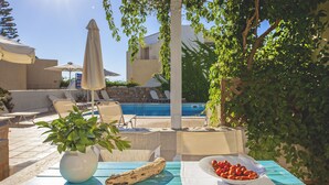 Un espace aménagé au bord de la piscine, avec des chaises longues, une table sur laquelle se trouve un saladier rempli de fruits et une plante en pot.