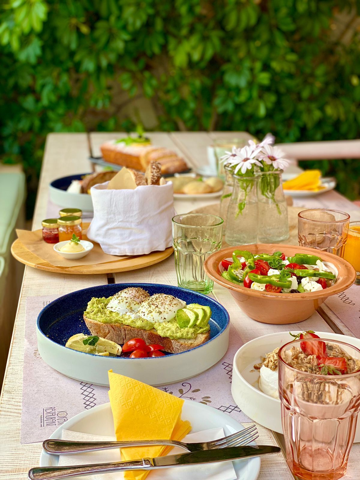 Una mesa dispuesta con varios platos, entre ellos tostadas con aguacate, una ensalada y un tazón de sopa.