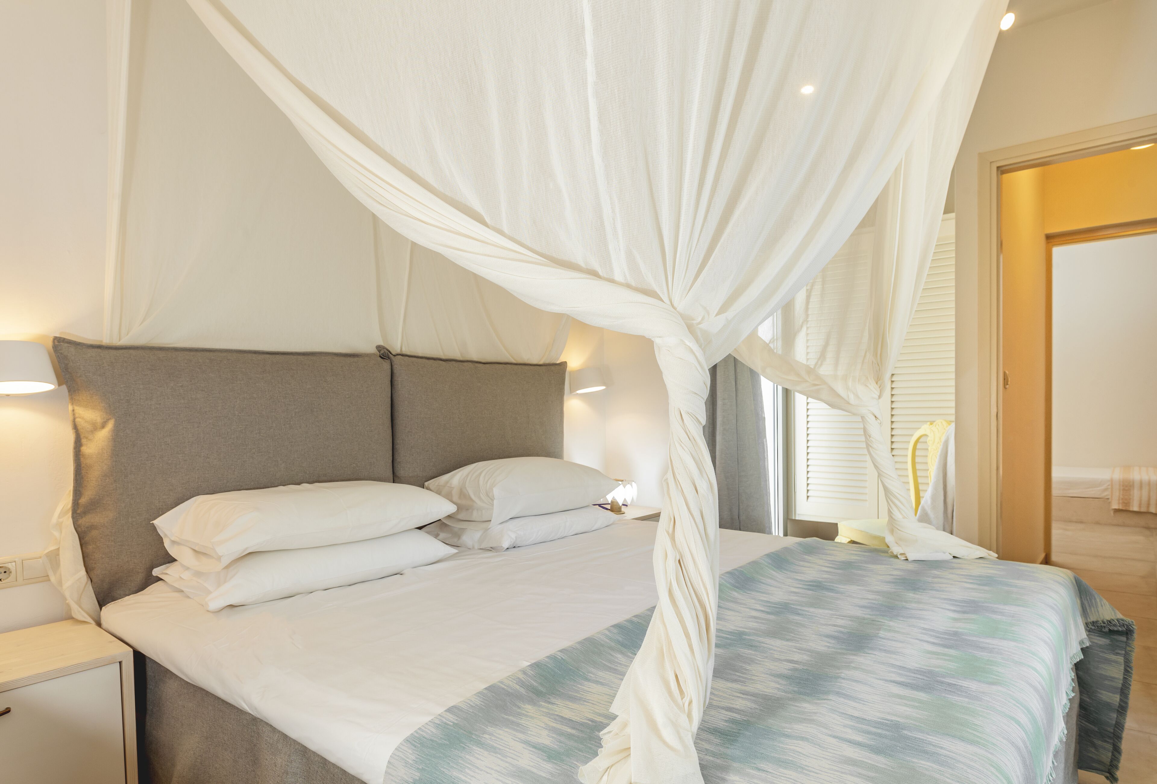 A bedroom with a bed, white curtains, and a nightstand.
