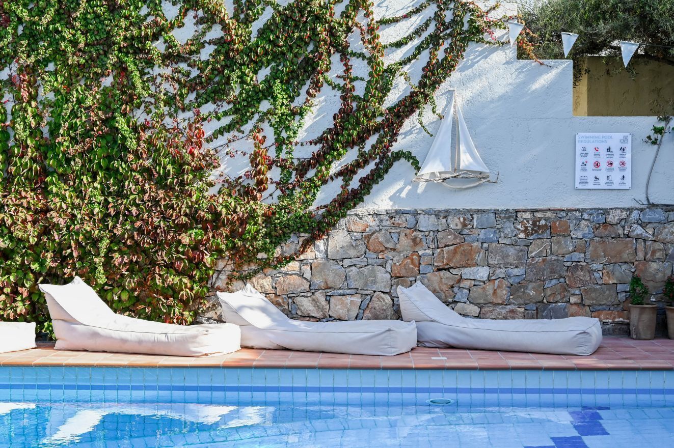 A swimming pool with lounge chairs, a stone wall, and a sign indicating pool regulations.