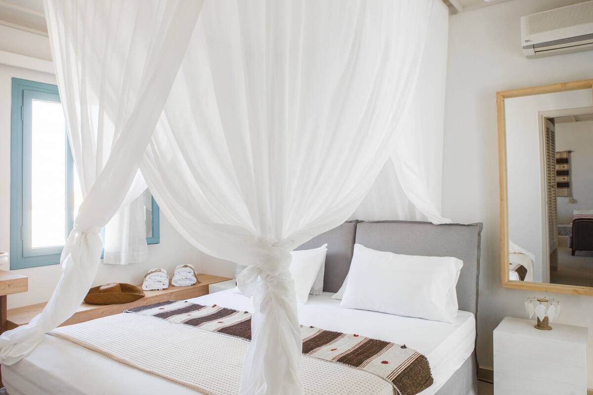 Un dormitorio con cama de dosel, una mesita de noche con lámpara y un espejo grande en la pared.