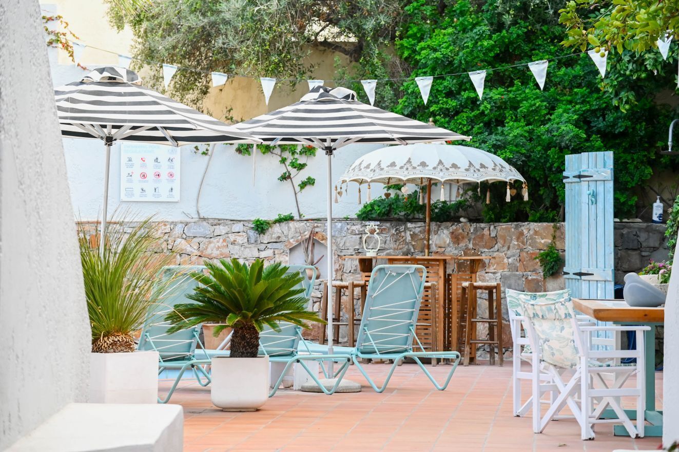 Un patio al aire libre con sombrillas a rayas, sillones de descanso y un muro de piedra de fondo.