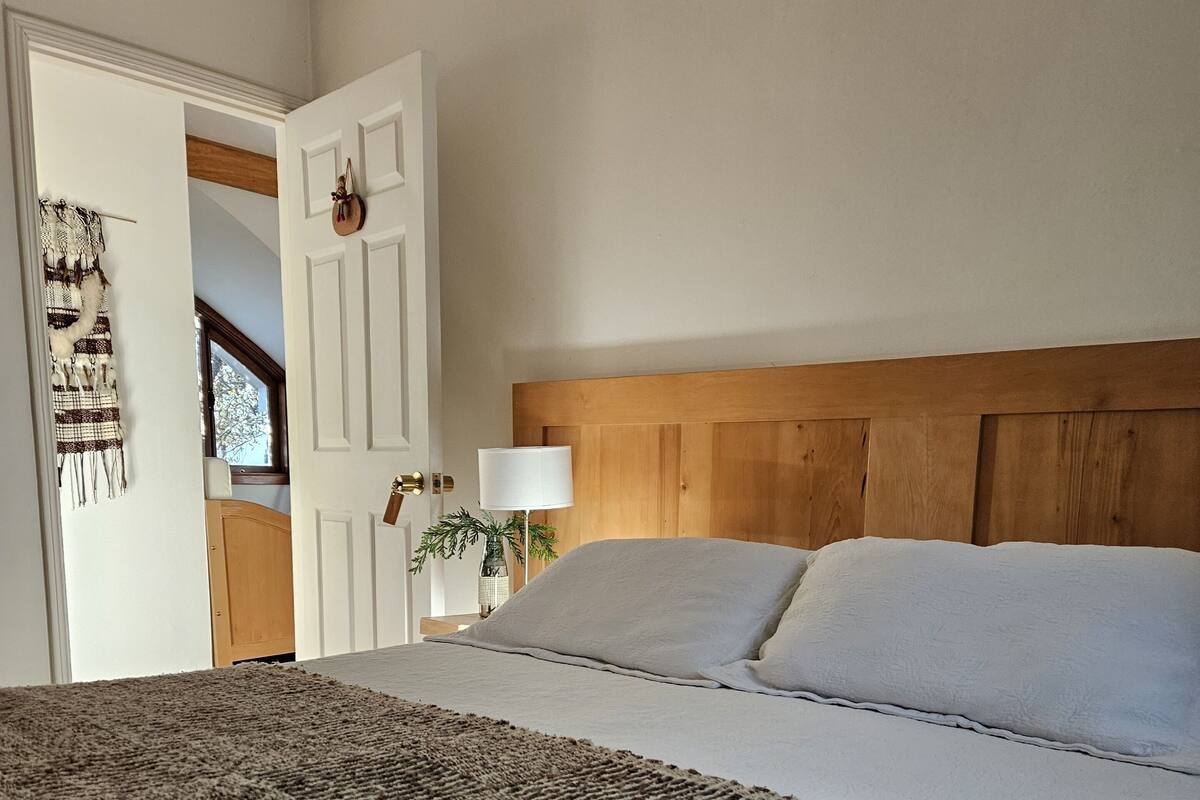 A bedroom with a large bed, a wooden headboard, a bedside lamp, and a door leading to another room.