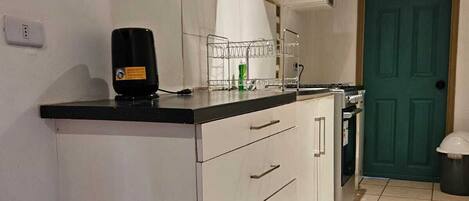 Una cocina con armarios blancos, encimera negra y puerta verde.