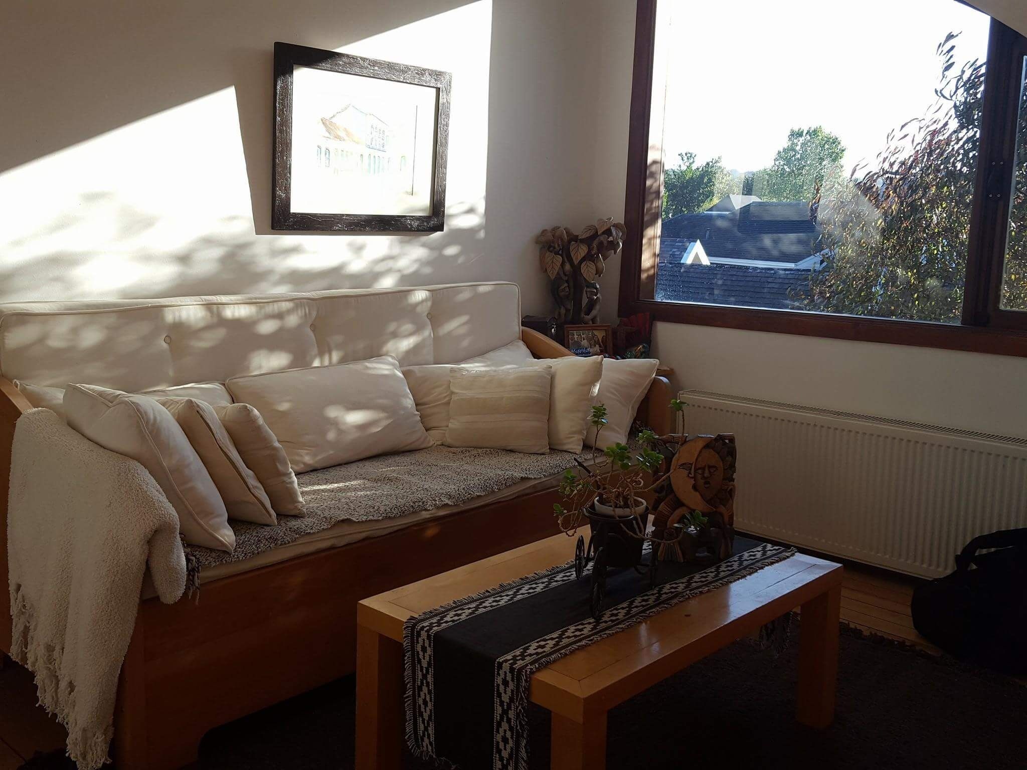 A living room with a sofa, a coffee table, and a window with a view of a house and trees.