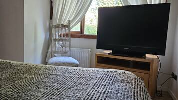 Une chambre à coucher avec un grand lit, un téléviseur posé sur un meuble en bois, un radiateur et une fenêtre avec des rideaux.