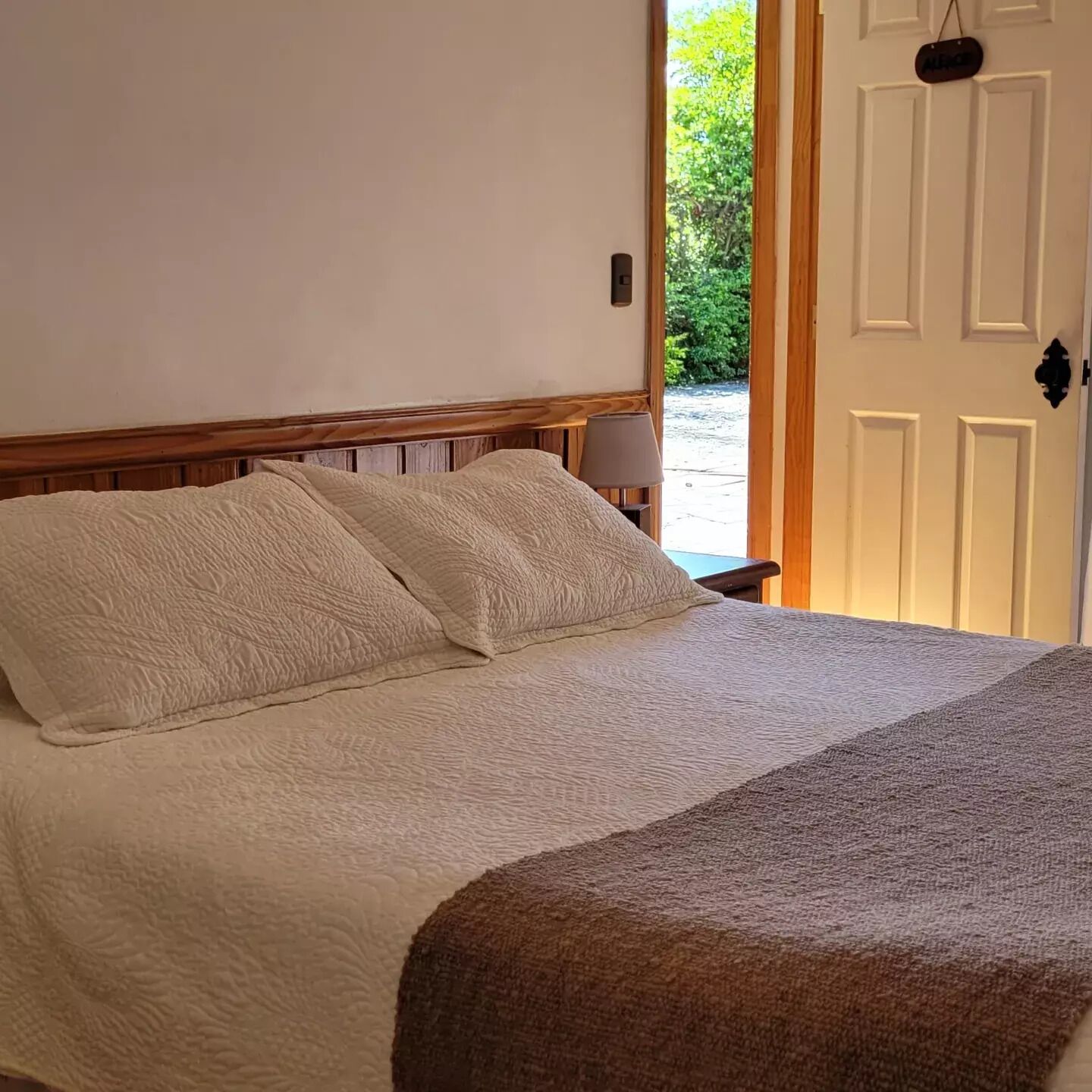 Una cama con cabecera de madera y colcha blanca con textura.