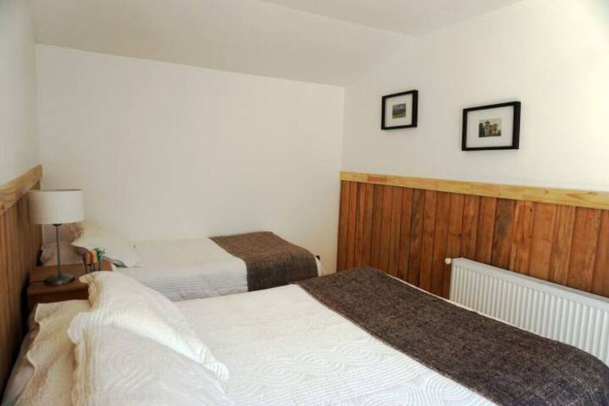 A hotel room with two beds, a wooden headboard, a radiator, and framed pictures on the wall.