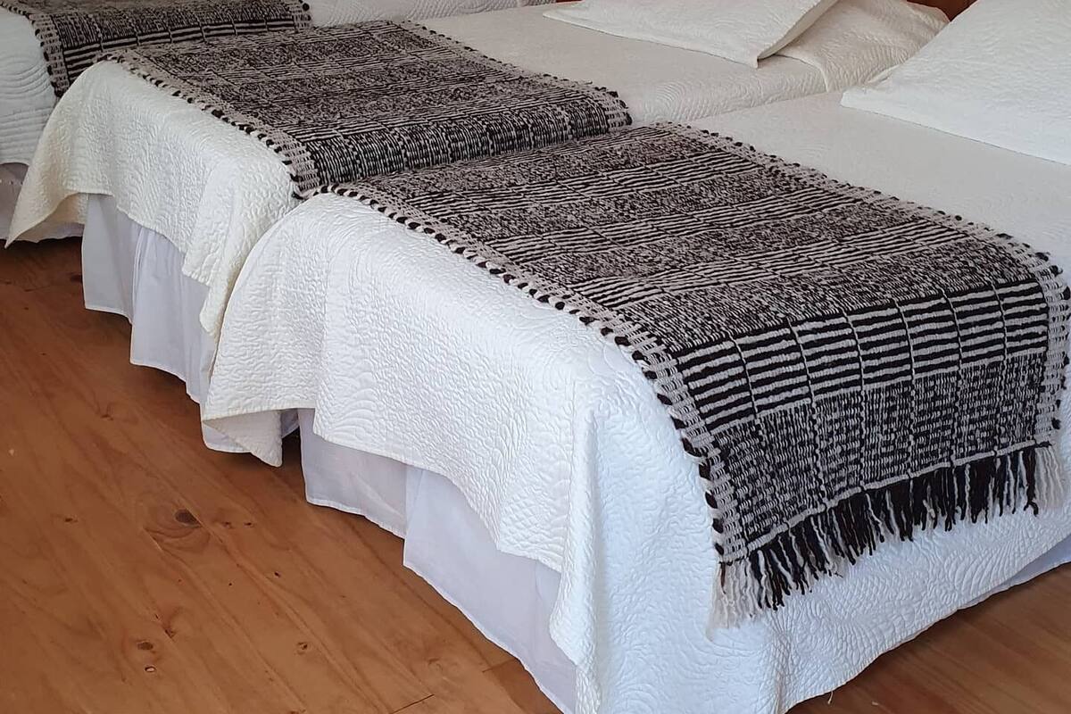 A hotel room with three beds, each with white bedding and a patterned throw blanket.