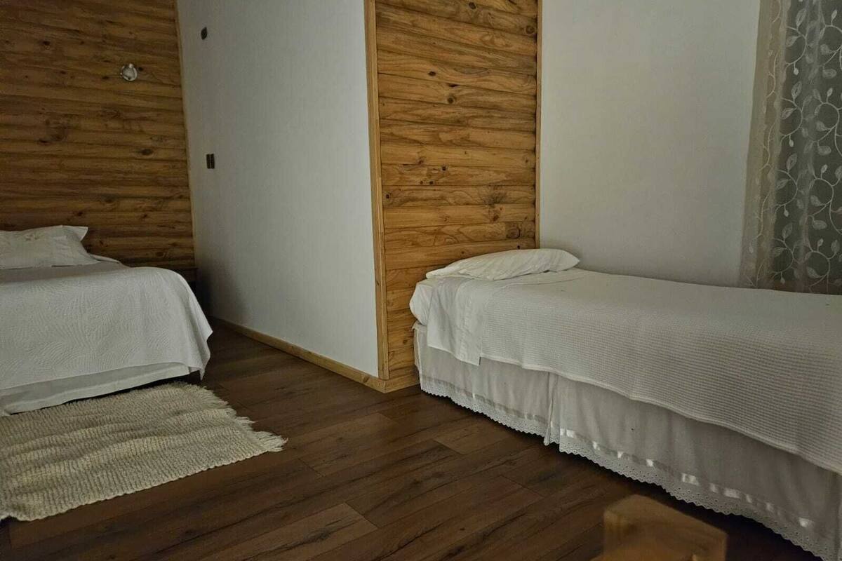 A room with two single beds, wooden panel walls, and a wooden floor.