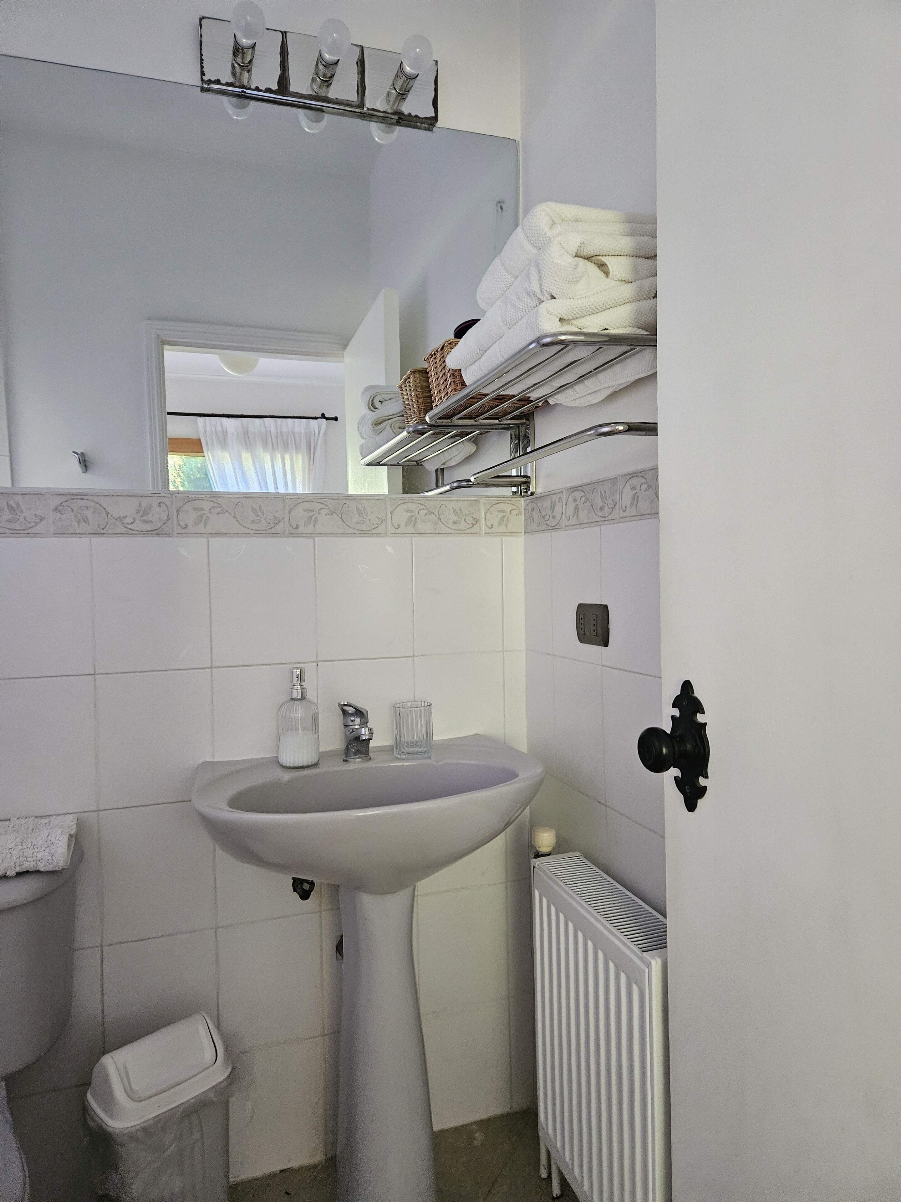 Une salle de bain avec un lavabo sur colonne, un porte-serviettes, un radiateur et une fenêtre avec des rideaux.