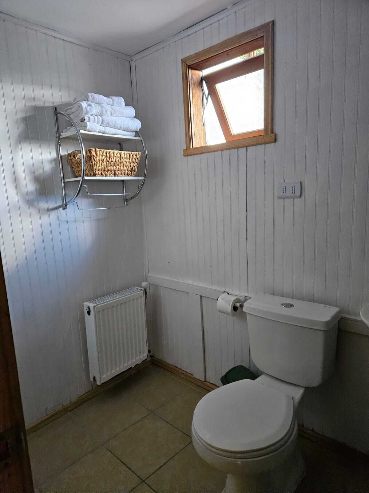 A small, basic bathroom with a toilet, a radiator, a towel rack, and a small window.