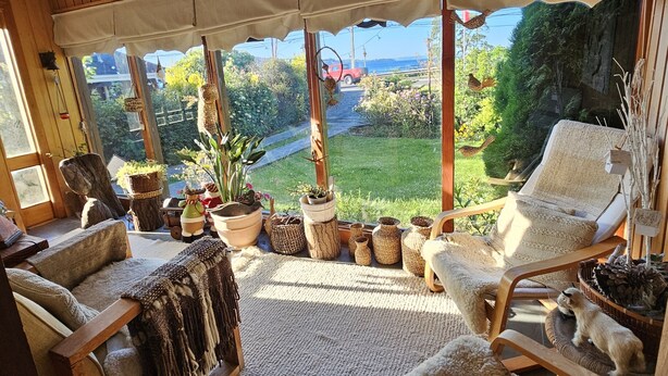 A cozy room with wooden walls, a curved ceiling, and large windows offering a view of a lush garden and the sea. - Canales del Sur (Puerto Varas)