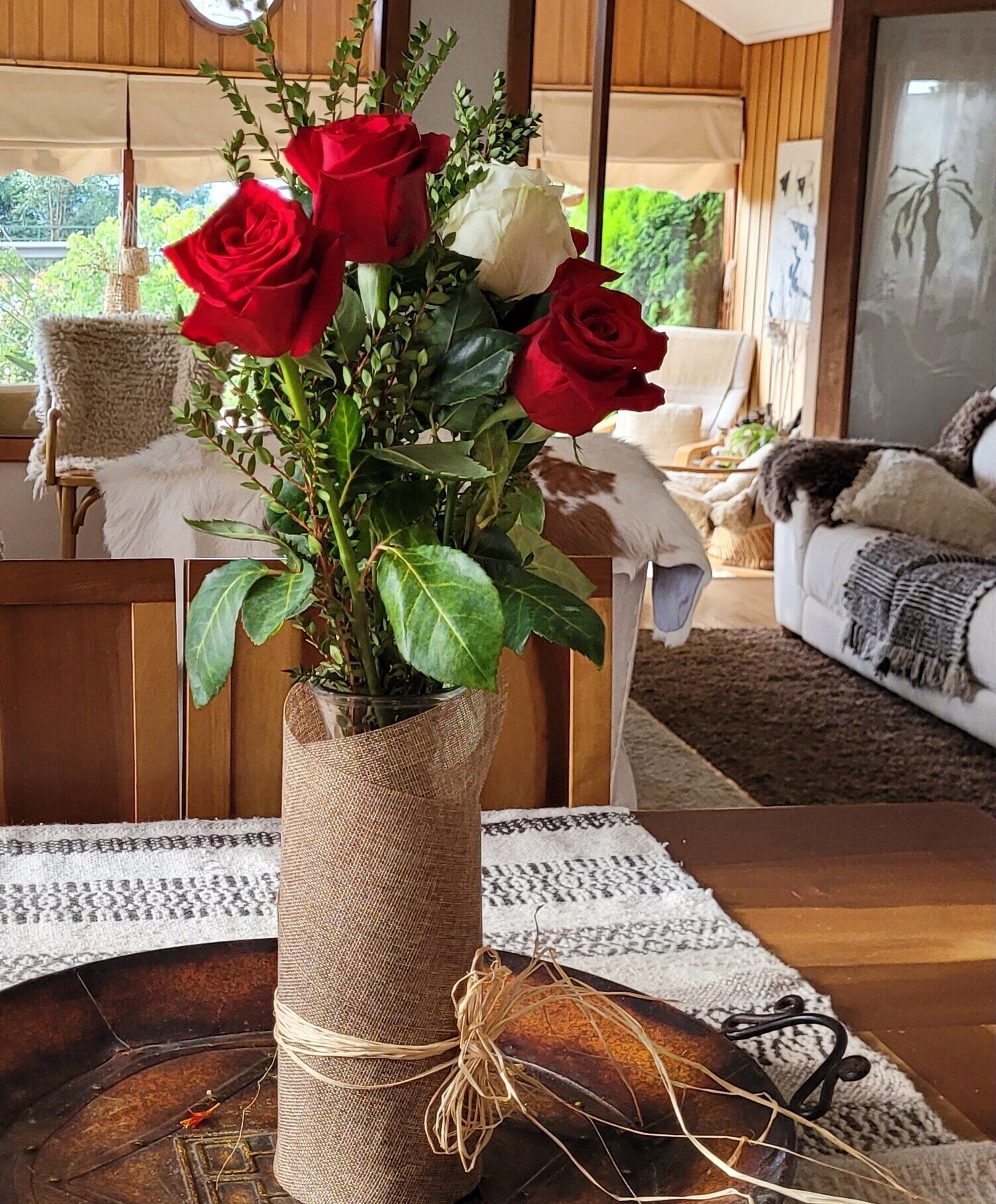 A rustic vase with red and white roses on a wooden table in a cozy living room.