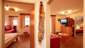 Une pièce comprenant un lit, un canapé rouge, une armoire en bois, un téléviseur et un manteau de fourrure accroché au mur.