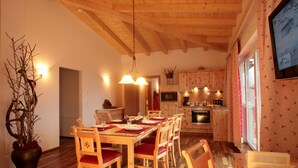 Un coin repas avec des meubles en bois, un lustre et une vue sur la cuisine.