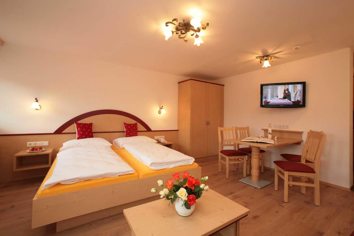 A hotel room with two beds, a desk with a chair, a television, and a vase of flowers.