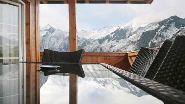 Une table en verre avec des chaises, dans un chalet en bois offrant une vue sur la montagne.