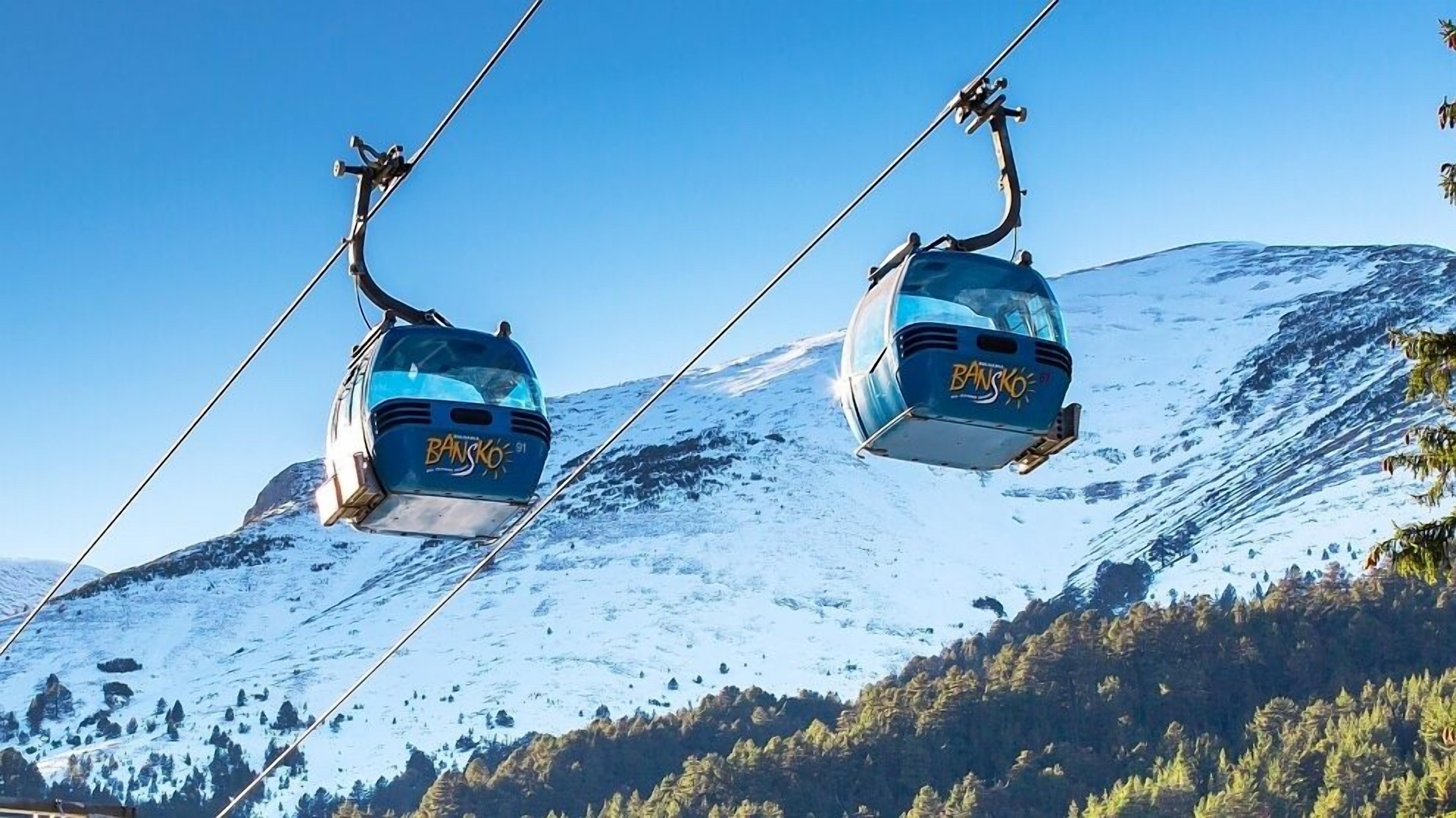 Dos telecabinas con la leyenda "BANSKO" suspendidas por cables frente a un paisaje montañoso nevado.