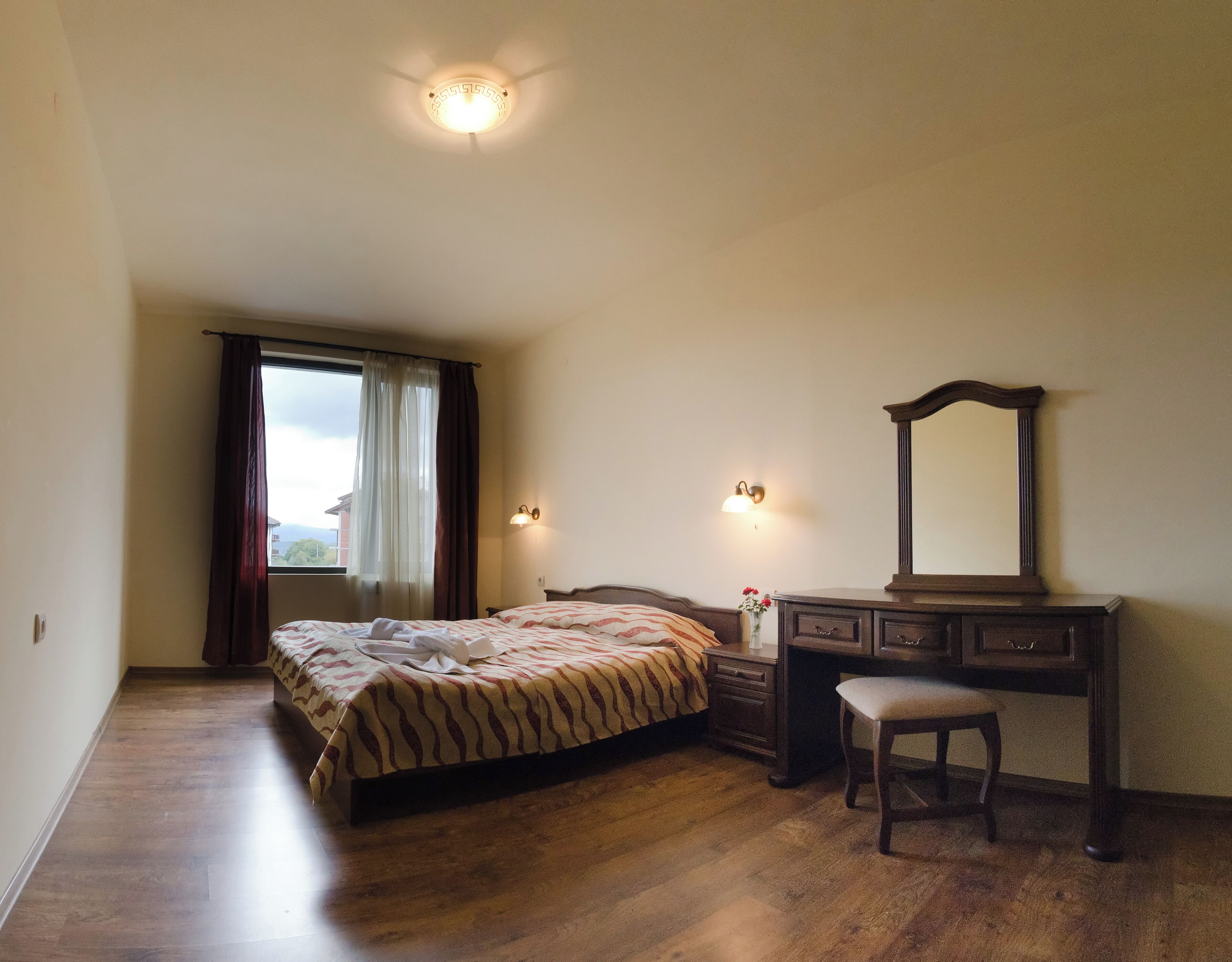 Een slaapkamer met een bed, een kaptafel, een spiegel en een raam met gordijnen.