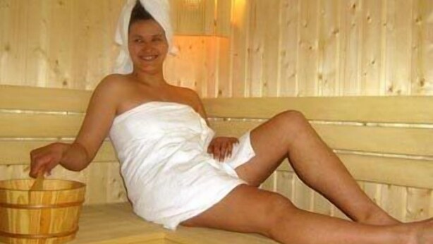 Een persoon zit op een houten bank in een sauna.