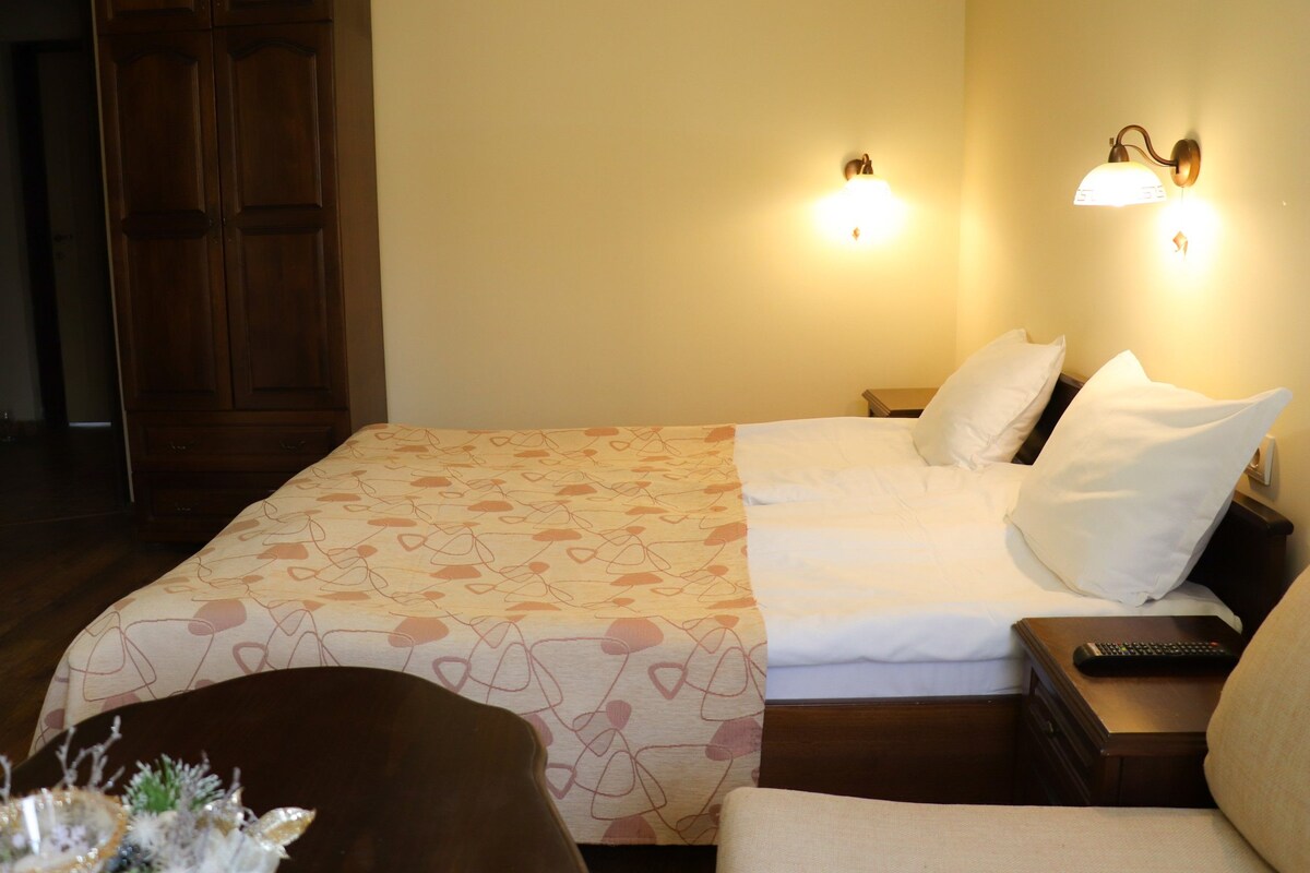 Une chambre d’hôtel comprenant un lit, deux lampes fixées au mur, une table de chevet avec une télécommande et une armoire en bois.