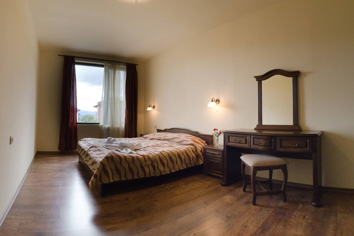 A bedroom with a bed, a dresser, a mirror, and a window with curtains.