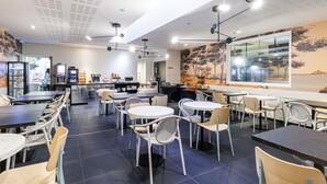 A modern cafe with multiple seating areas, including tables and chairs, and a kitchen visible in the background. - Aparthotel Adagio Nice Centre (Nice)