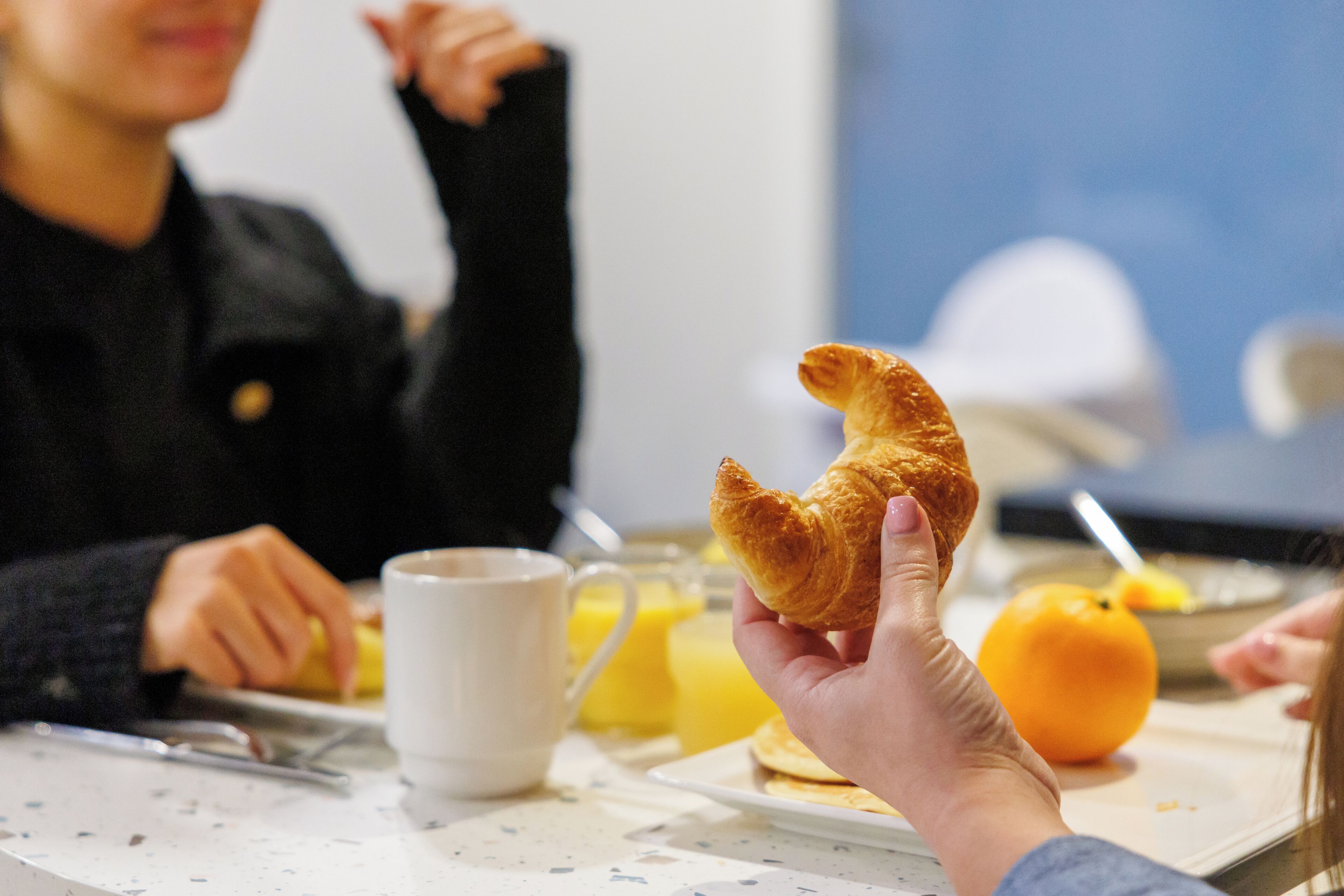 A breakfast setting with a croissant, orange, and a cup of coffee on a table.