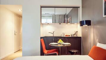 Una habitación de hotel moderna con una cama, una mesa de comedor con sillas, una pequeña cocina y una lámpara de noche.