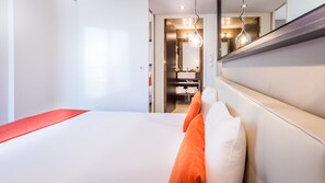 Een hotelkamer met een groot bed, een rode decoratieve kussen, een wit hoofdeinde, en een spiegel boven het bed.