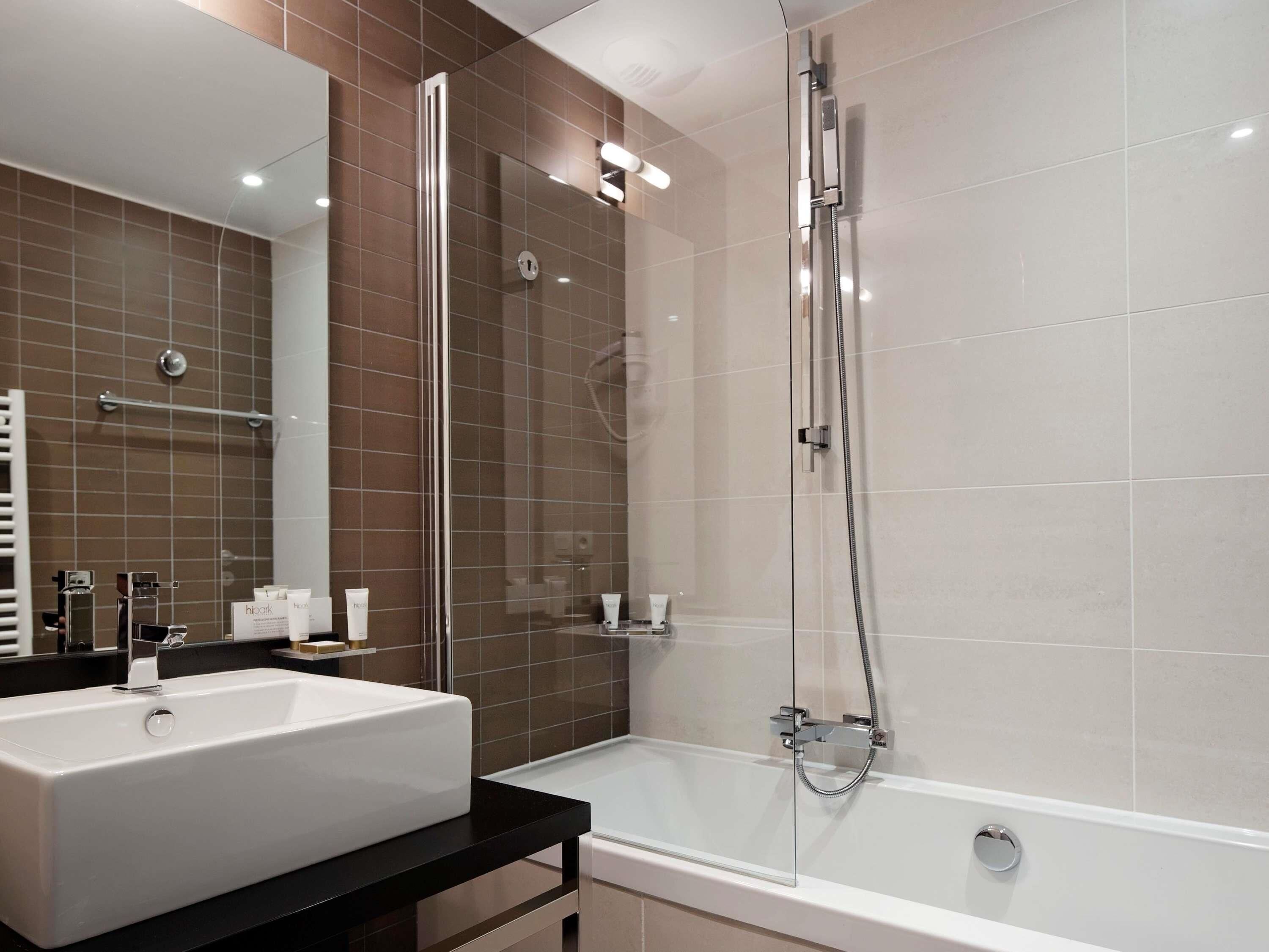 A modern bathroom with a large mirror, a white sink, a bathtub, and a glass-enclosed shower.
