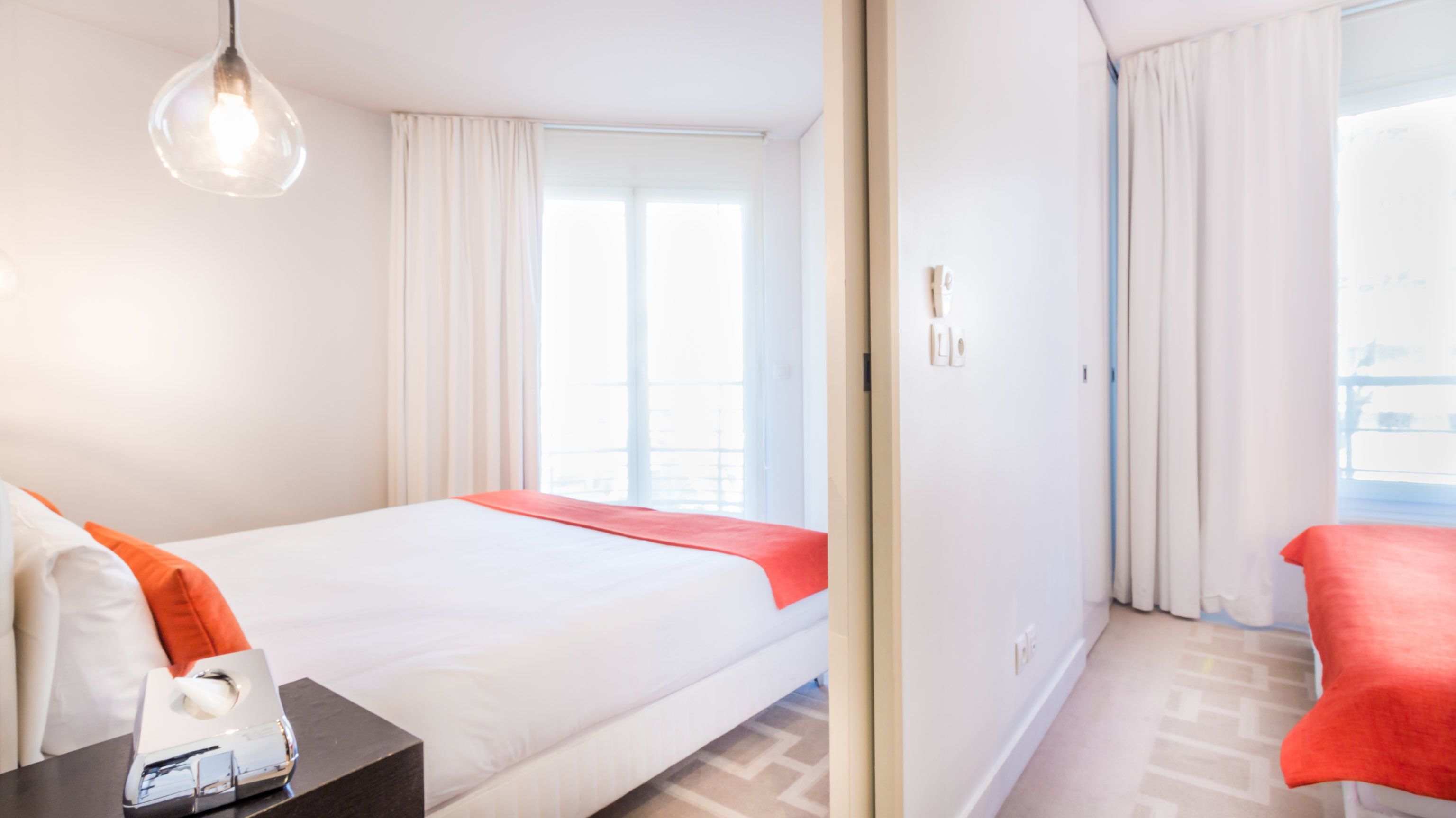 Une chambre d’hôtel avec un lit, une table de chevet avec une boîte de mouchoirs, une fenêtre avec des rideaux et une vue sur l’extérieur.