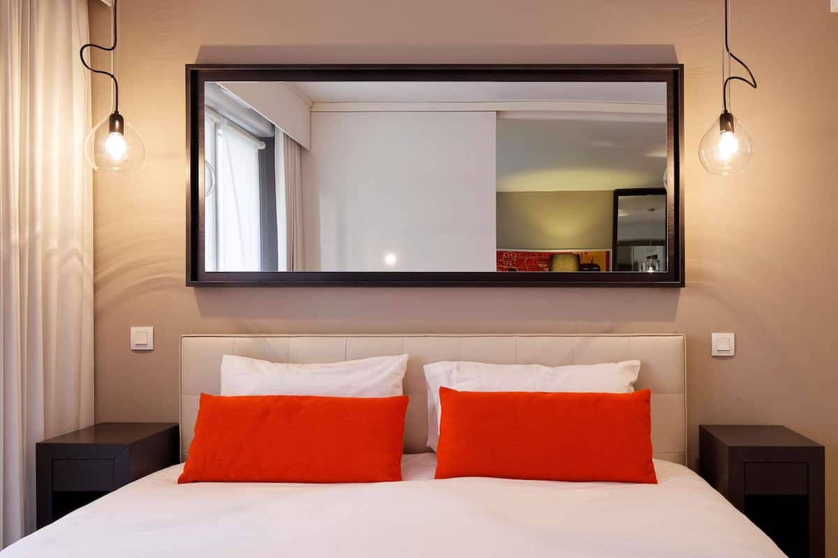 Ein Hotelzimmer mit einem großen Spiegel, zwei weißen Betten mit orangefarbenen Kissen und zwei Nachttischen.
