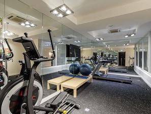 Une salle de sport équipée de tapis de course, de ballons d’exercice et de murs recouverts de miroirs.
