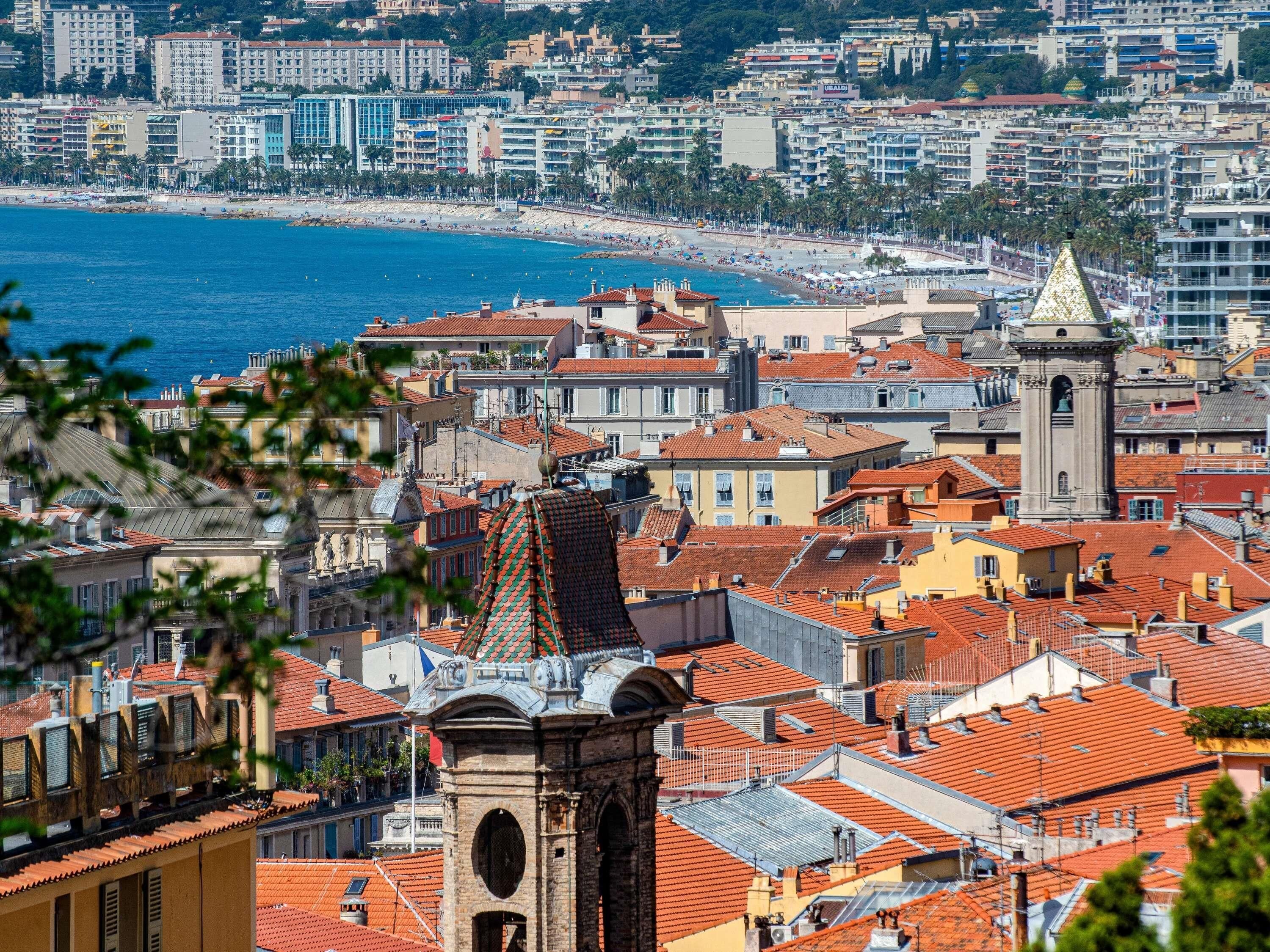 Un paisaje urbano costero con una torre destacada, edificios urbanos densos y una playa al fondo.