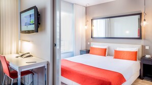 A hotel room with a bed, a desk, a chair, a TV mounted on the wall, and a bedside table with a lamp. - Aparthotel Adagio Nice Centre (Nice)
