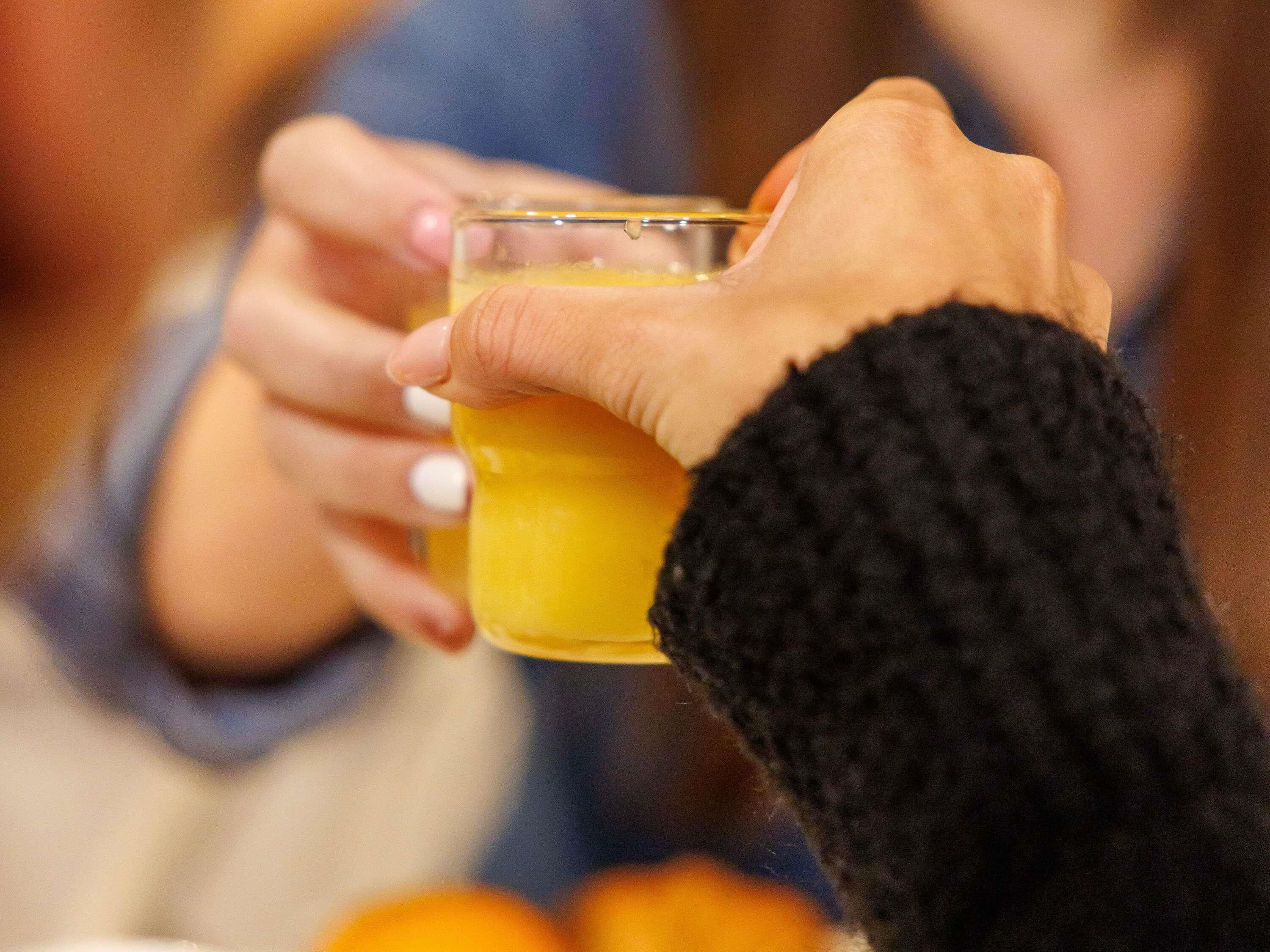 Iemand houdt een glas sinaasappelsap vast.