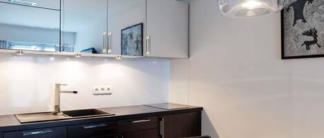 A modern kitchen with a dark countertop, white cabinets, a stainless steel sink, and a dining area with a table and chairs.