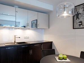 Een moderne keuken met een donker aanrecht, witte kasten, een roestvrijstalen spoelbak en een eethoek met een tafel en stoelen.