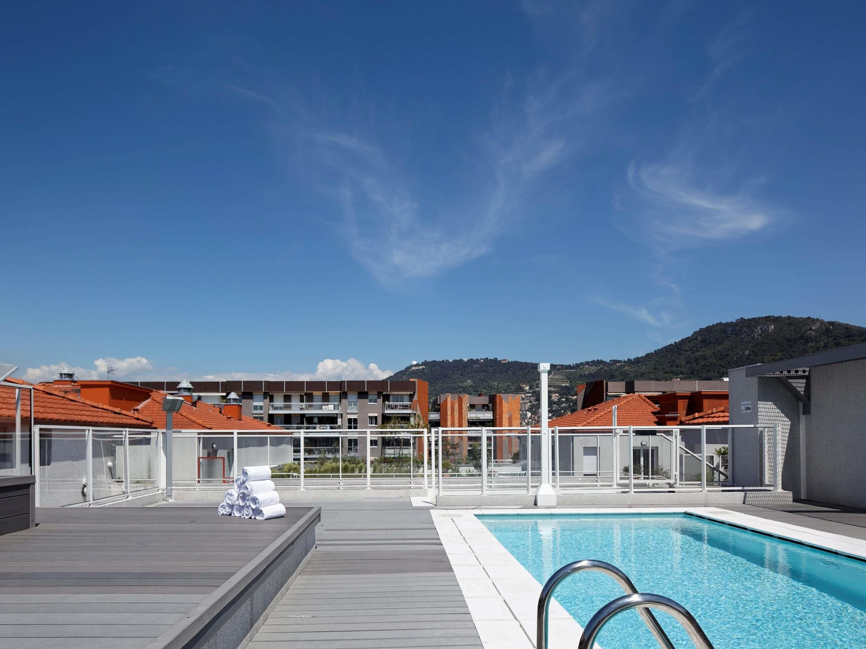Piscina no terraço com vista clara para edifícios e uma montanha ao fundo.