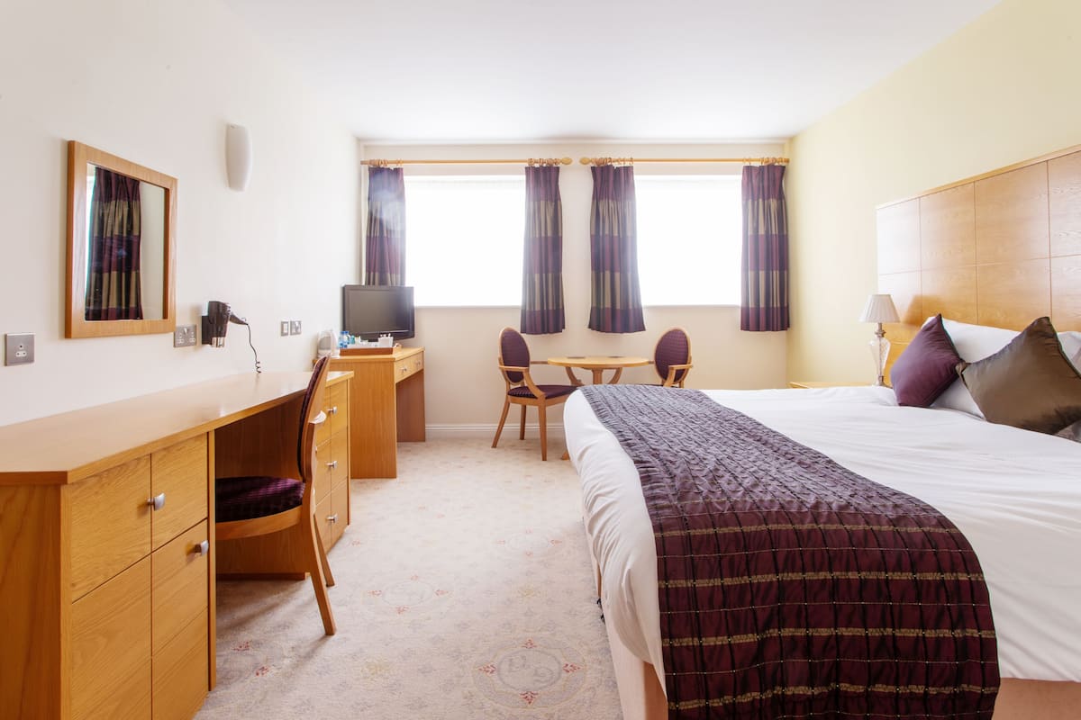 A hotel room with a bed, desk, chair, television, and curtains.
